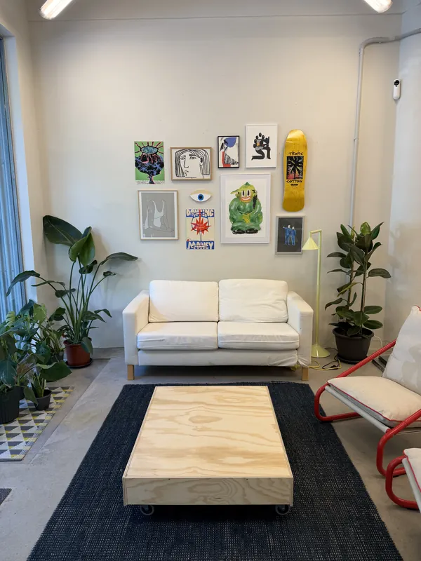 Chill zone at Espacio Remoto: white sofa, plywood coffee table, plants and a wall full of prints