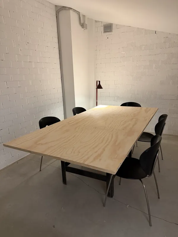 Meeting room at Espacio Remoto: large plywood table, black chairs and a red floor lamp